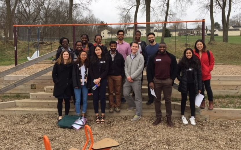 12 students and three staff members standing in a playground in front of a swing set