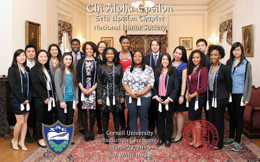 large group of students and staff dressed in professional attire wearing blue and white chords standing in a great hall at the AD White House on Cornell’s campus