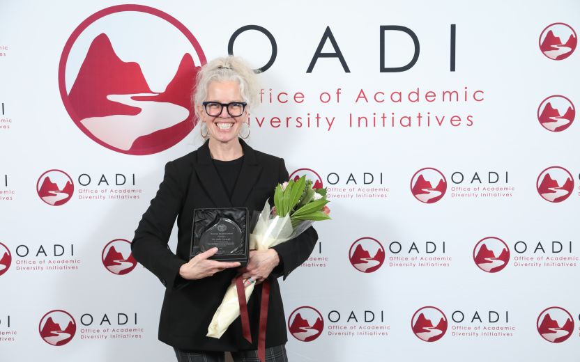 Julie Carmalt is smiling at the camera. She is standing In front of a OADI backdrop and is holding flowers and her award