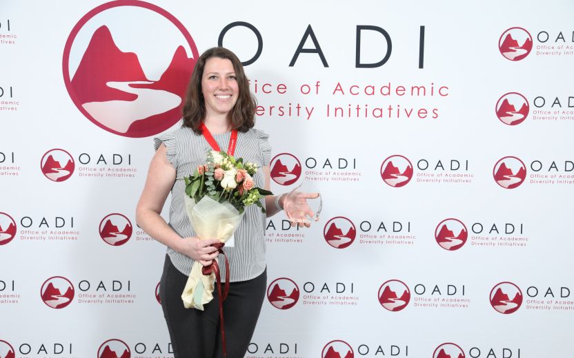 Jennifer Houtz is smiling and standing with a bouquet of flowers in one hand and her award in the other hand