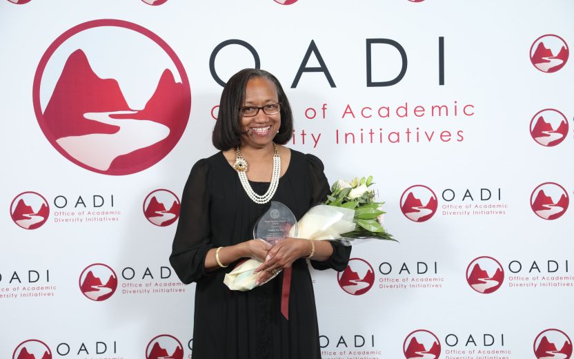 Nadine Porter is standing in front of a OADI banner.  She is smiling and holding a bouquet of flowers and her award