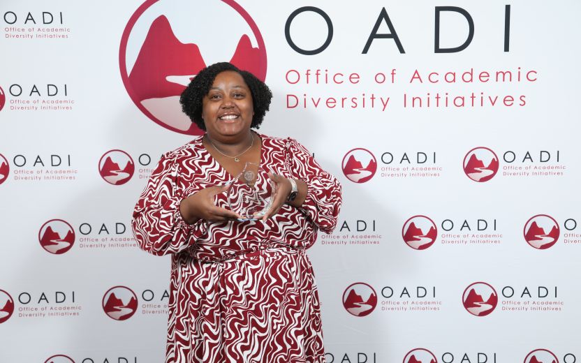 Misha N. Inniss-Thompson is standing in front of a OADI backdrop and is smiling and holding her award.