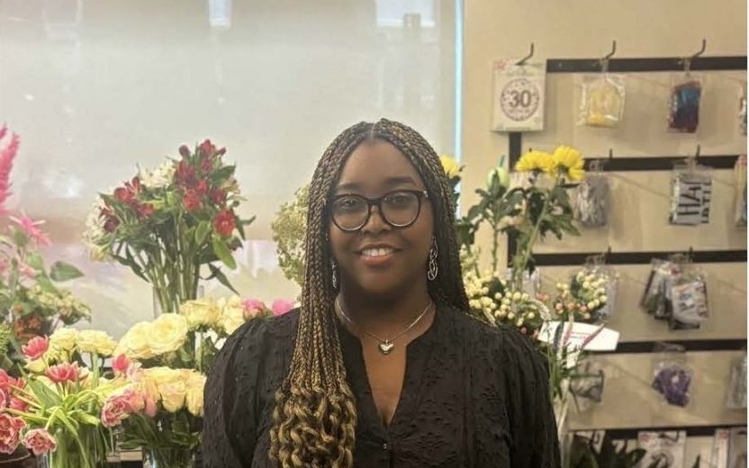 Danielle Iringe-Koko is smiling at the camera. She has on a black dress and is in a room of flowers