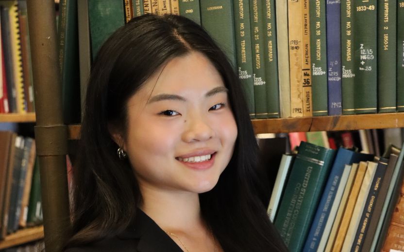 Lin Kuang is sitting in a library and smiling at the camera 