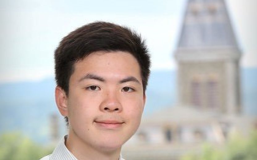 Kyler Lin is smiling at the camera. McGraw tower at Cornell is in the background