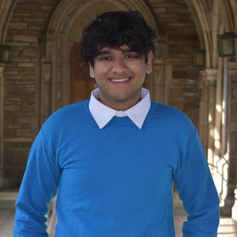 Photo of Mo in a blue sweater standing in the archway of West Campus on Cornell University Campus