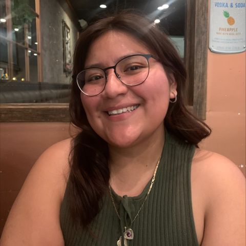 Chelsea Tenezaca sitting down smiling, she is wearing a green shirt and has glasses