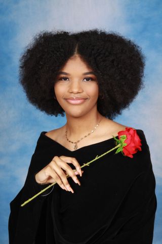 Cheyanne is smiling at the camera.  She is wearing a black dress and is holding a rose in her hand
