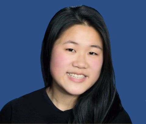 Ashley Yang is smiling at the camera. There is a blue background, and she has on a black shirt