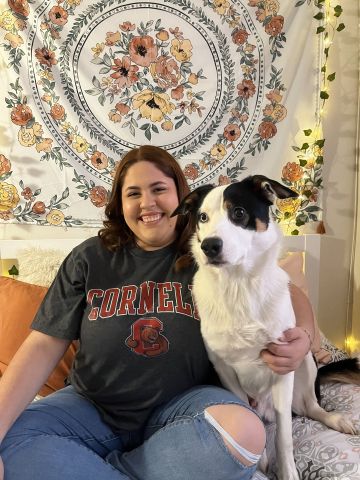 Rosalynn Silva is sitting and smiling at the camera. She has on a Cornell T-shirt and is with her dog