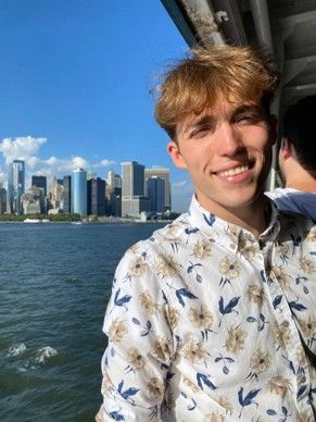 Gabriel Garcia is smiling at the camera and is on a ferry boat with a city skyline in background