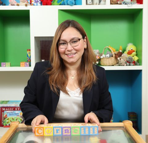 Fatima Martinez is in a childrens classroom. She is snmiling at the camera and holding blocks that spell Cornell