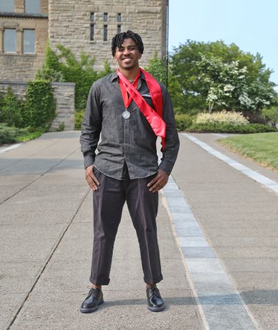 Kellen Cooks is smiling at the camera he is outside by the clocktower on Cornell campus