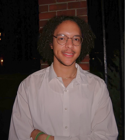 Justin Taveras is smiling at the camera. He has on a white button down shirt and glasses