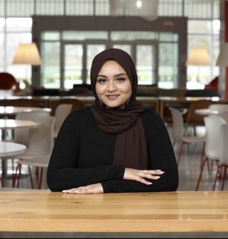 Nuzhat Mukul is smiling at the camera. She is seated with her hands folded and has on professional clothes