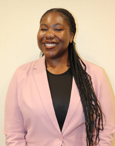 Ruth Osagie is wearing a pink blazer and is smiling at the camera