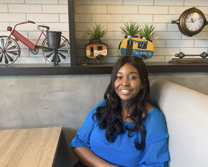 Danielle Iringe-Koko is sitting down and smiling at the camera, She has on a blue shirt