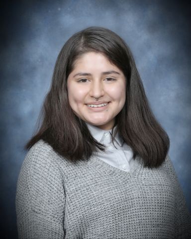 Mayra Miranda is smiling at camera has on a sweater and collar underneath