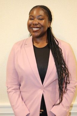 Ruth Osagie is smiling at the camera. She has on a pink blazer