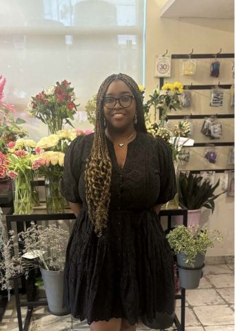 Danielle Iringe-Koko is smiling at the camera. She has on a black dress and is in a room of flowers