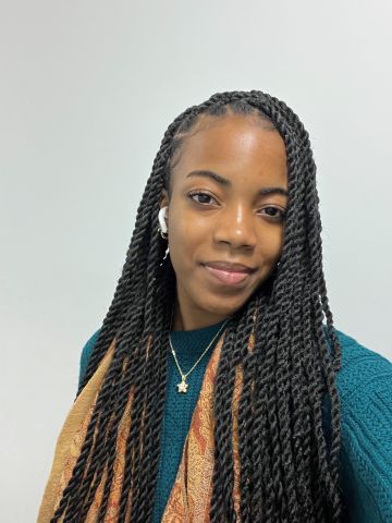 Dijonay Mills is smiling at the camera. She has on a blue sweater and brown scarf