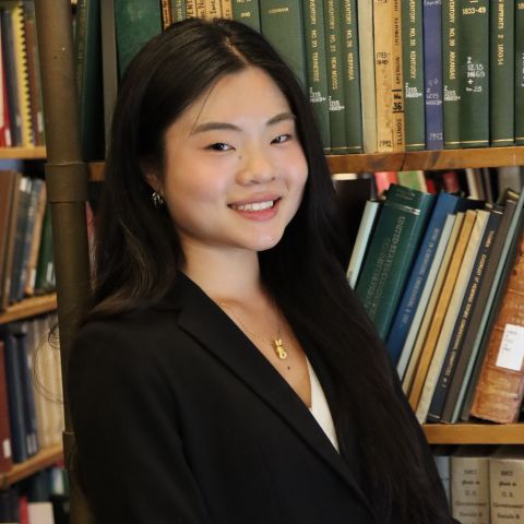 Lin Kuang is smiling at the camera, with professional clothes on. She is in a library 