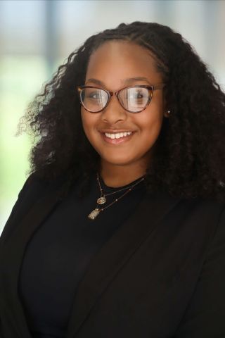 Marley Diallo is smiling at the camera. She has on glasses and a black outfit