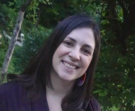 Gabrielle Smith is standing outside near some woods and is smiling at the camera