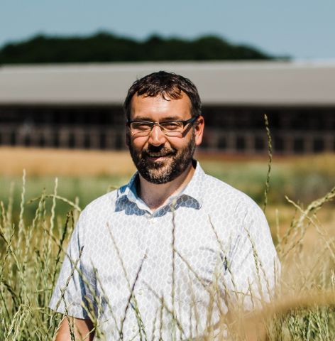 Matt Ryan is smiling at the camera. He is standing outside in a field on a nice day