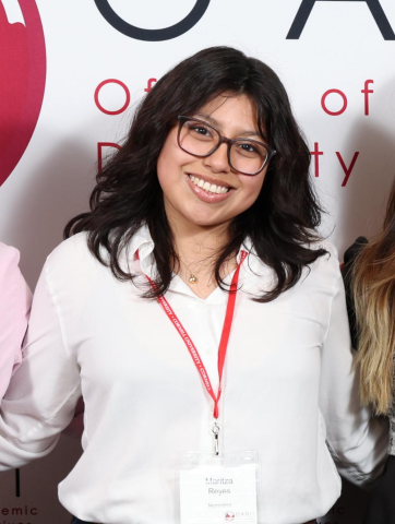 Photo of Maritza in a while blouse with a nametag on in front of the OADI step and repeat.