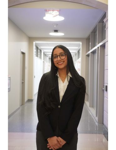 Gabriela Romero is smilign at the camera. She is wearing professional clothes and standing in a hallway