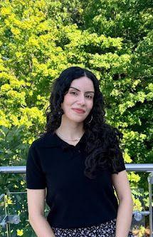 Cagla Duman is smiling at the camera. Sher is outside on a sunny summer day.