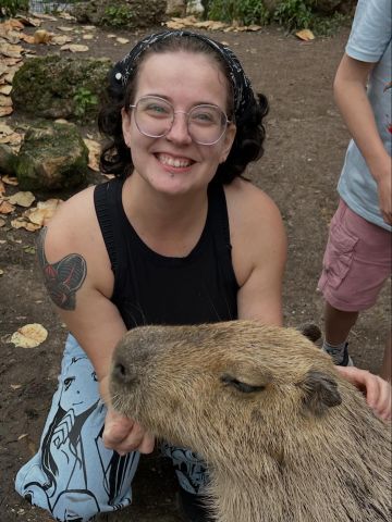 Diane Stonestreet is smiling at the camera. She is feeding a capybara animal.
